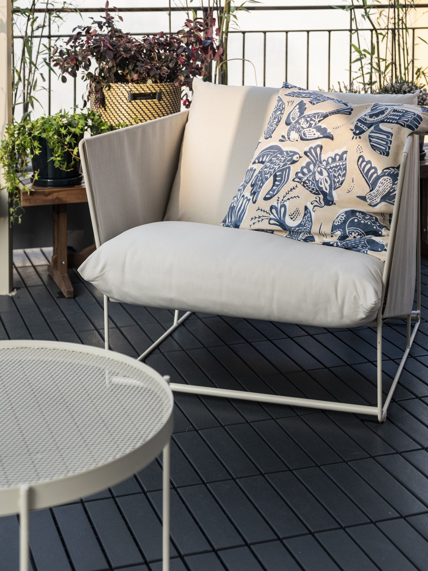 Terrazzo con poltrona da esterno HAVSTEN e cuscino con motivo di uccelli bianco e blu e davanti una tavolino beige KROKHOLMEN.