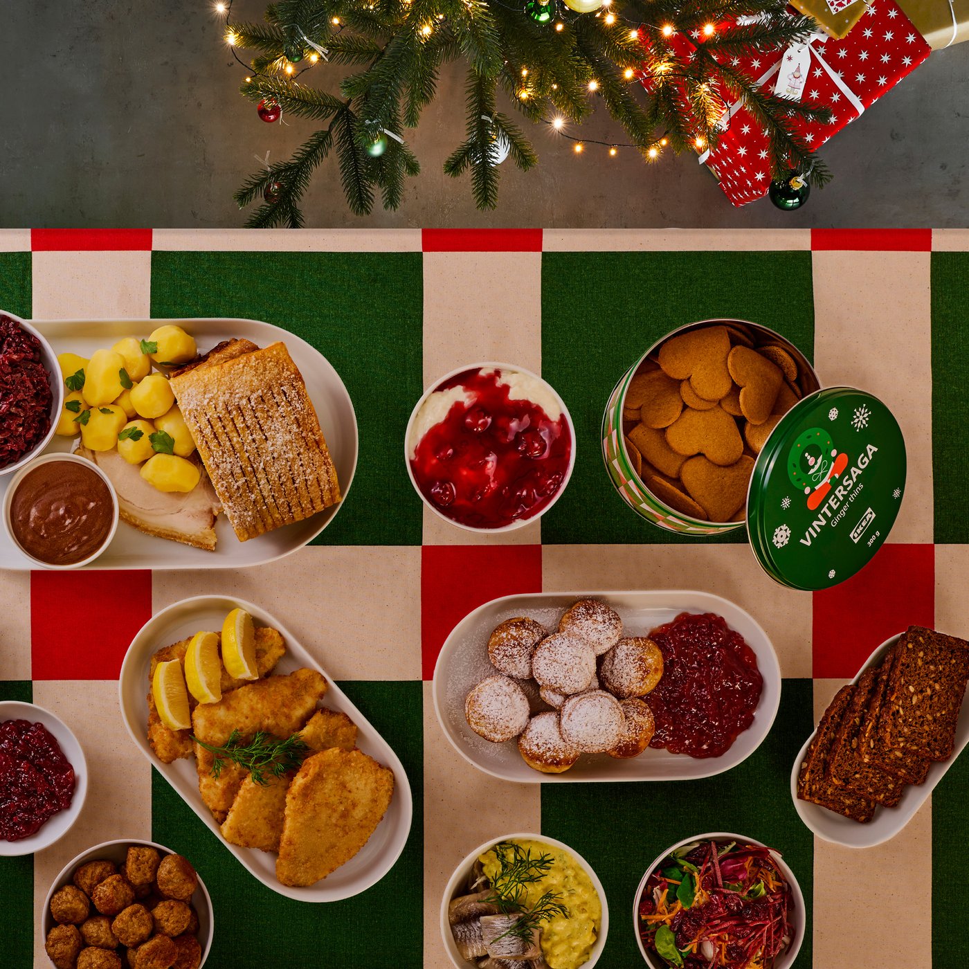 Oversigtsbillede af et julebord dækket med en VINTERFINT dug i røde og grønne tern. På bordet står en masse juleretter på hver deres tallerken.