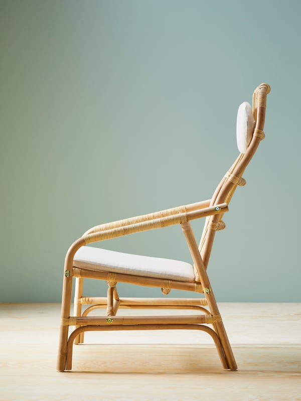 Vue latérale d’un fauteuil en rotin SALNÖ avec jeu de coussins GRYTTOM dans une pièce avec un sol en bois et des murs gris/vert.