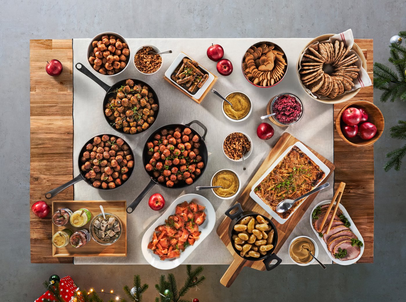 Julbord med klassiska rätter som knäckebröd, äpplen, skinka, köttbullar och såser, uppdukat på ett träbord i bufféstil.