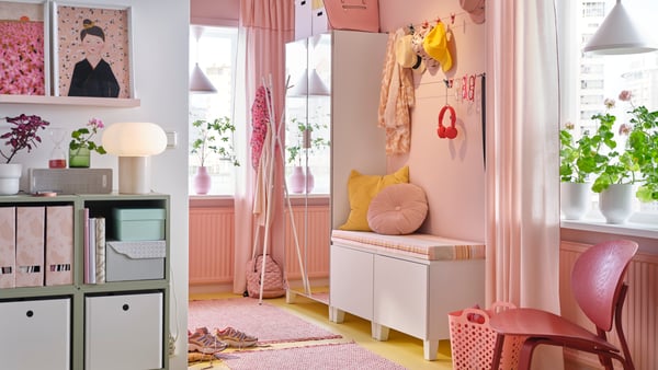 En rosa hall med PLATSA spegelgarderob, bänk med rosa och gula kuddar, en rosa matta och hängande mössor och halsdukar.