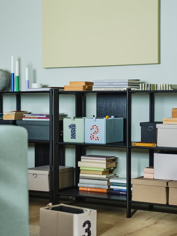 Black JÄTTESTA shelving units are placed against a light blue wall, with BARNDRÖM boxes and books on its shelves.