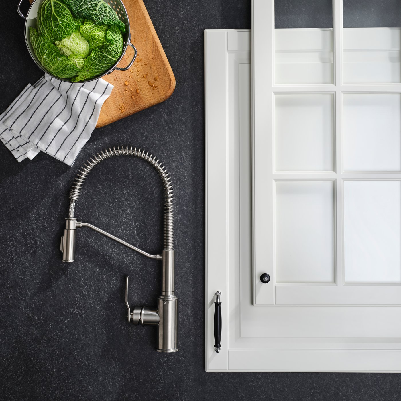 A close-up of a TAKSJÖN pull-down mixer tap in stainless steel colour, set against a white traditional kitchen combination.