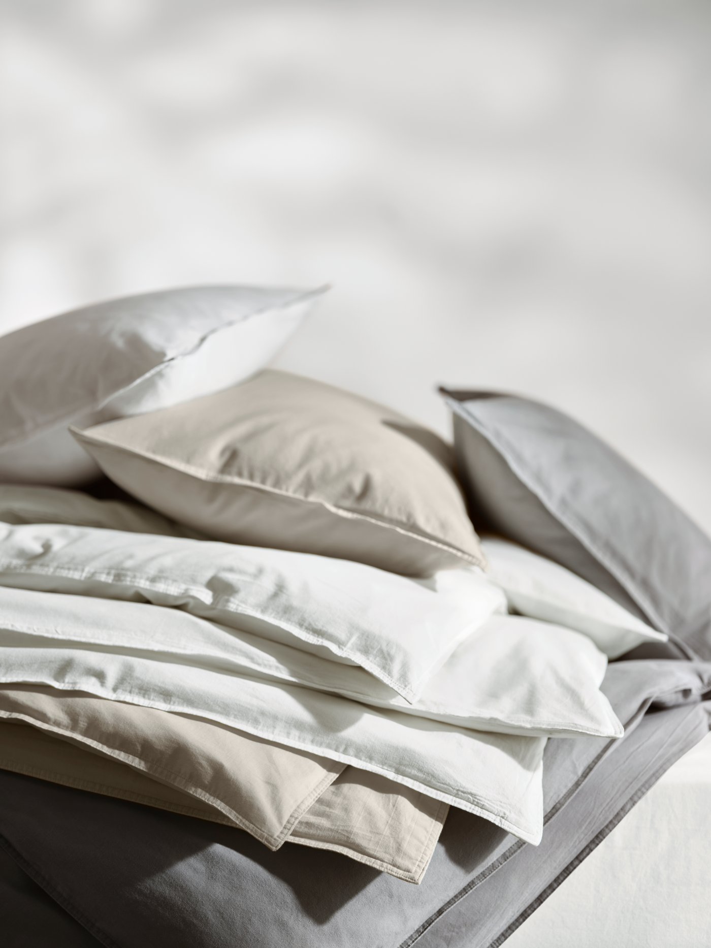 A pile of neutral-coloured bed linen includes a white, 100% cotton ÄNGSLILJA duvet cover and pillowcase.