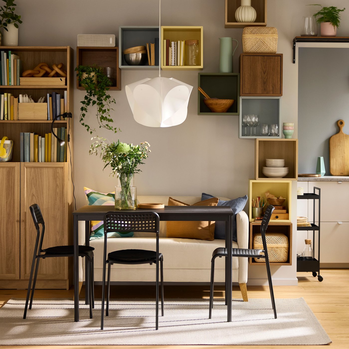 Ein schwarzer SANDSBERG Tisch, drei Stühle und ein Sofa stehen in einem Wohnzimmer. Im Hintergrund befindet sich ein BILLY Bücherregal.