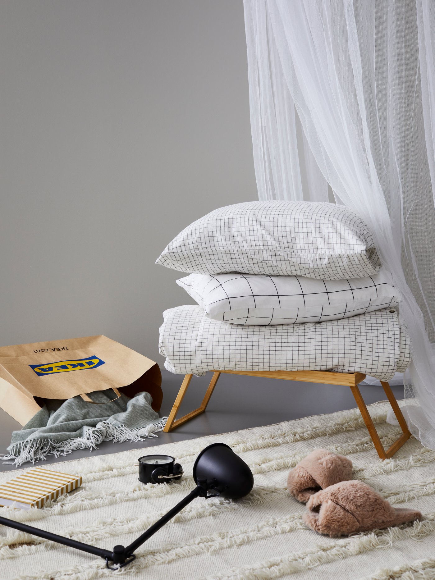 Die ÅKERFIBBLA Bettwäsche liegt hier auf einem RESGODS Tabletttisch. In der Nähe sind eine IKEA Tasche, ein HOLMVI Plaid, eine SKURUP Wand-/Arbeitsleuchte und eine DEKAD Uhr zu sehen.