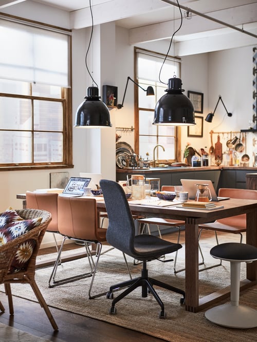 Dining area featuring a table, two pendant lamps, a brown chair, a beige chair, a conference chair, and a standing support.