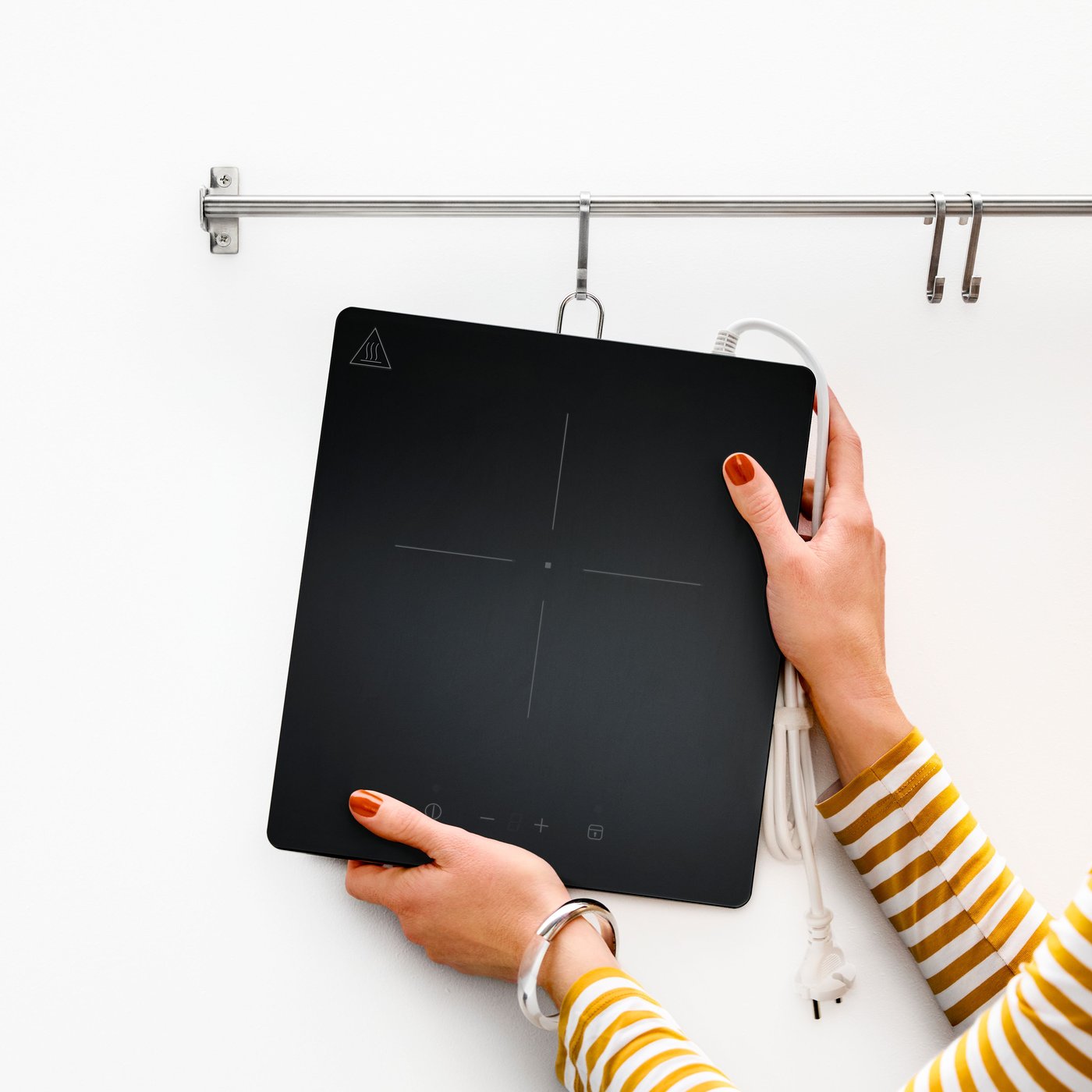 A close-up of hands holding a white TILLREDA portable induction hob with a single cooking zone and a power cord.