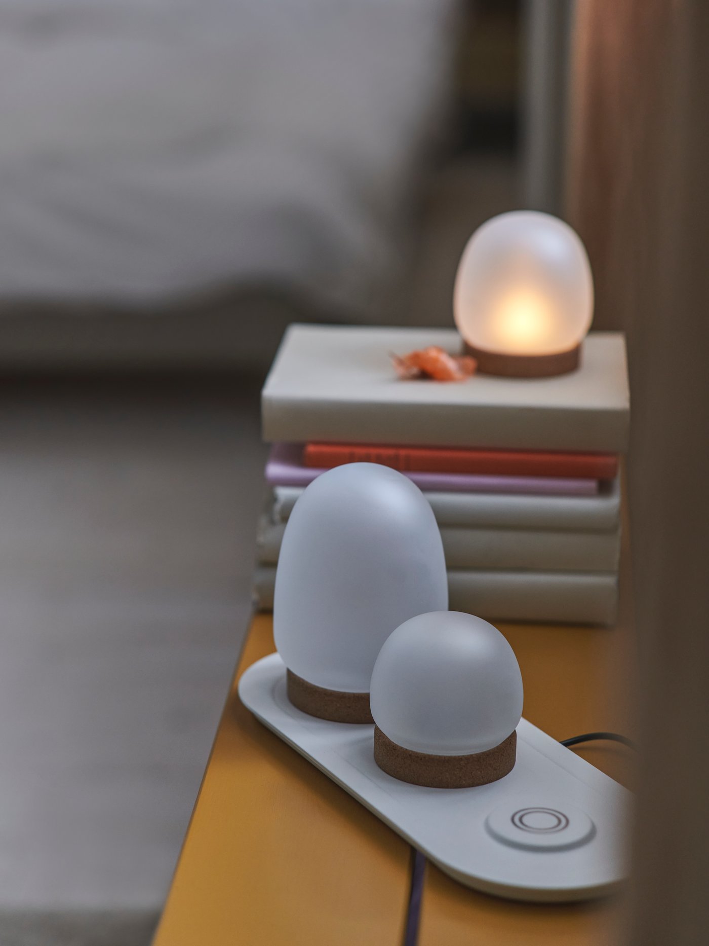 Three lamps from the 4-piece PRAKTSPIREA LED decoration lighting set. Two are on a charging tray and one is on some books.
