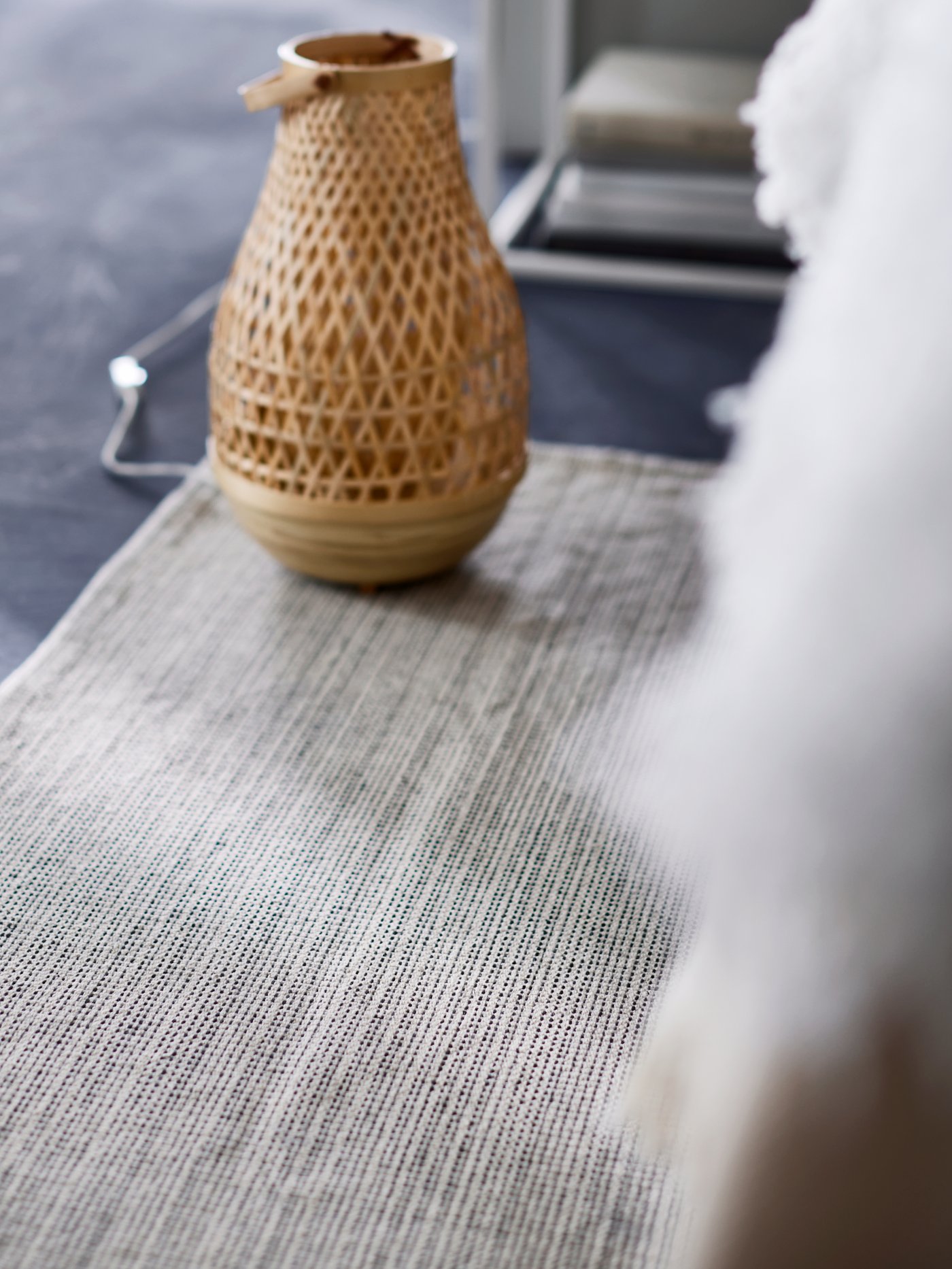 Suelo de dormitorio con alfombra beige de tejido liso y lámpara de mesa hecha a mano con fibras de bambú tejidas, base de bambú y asa de bambú.