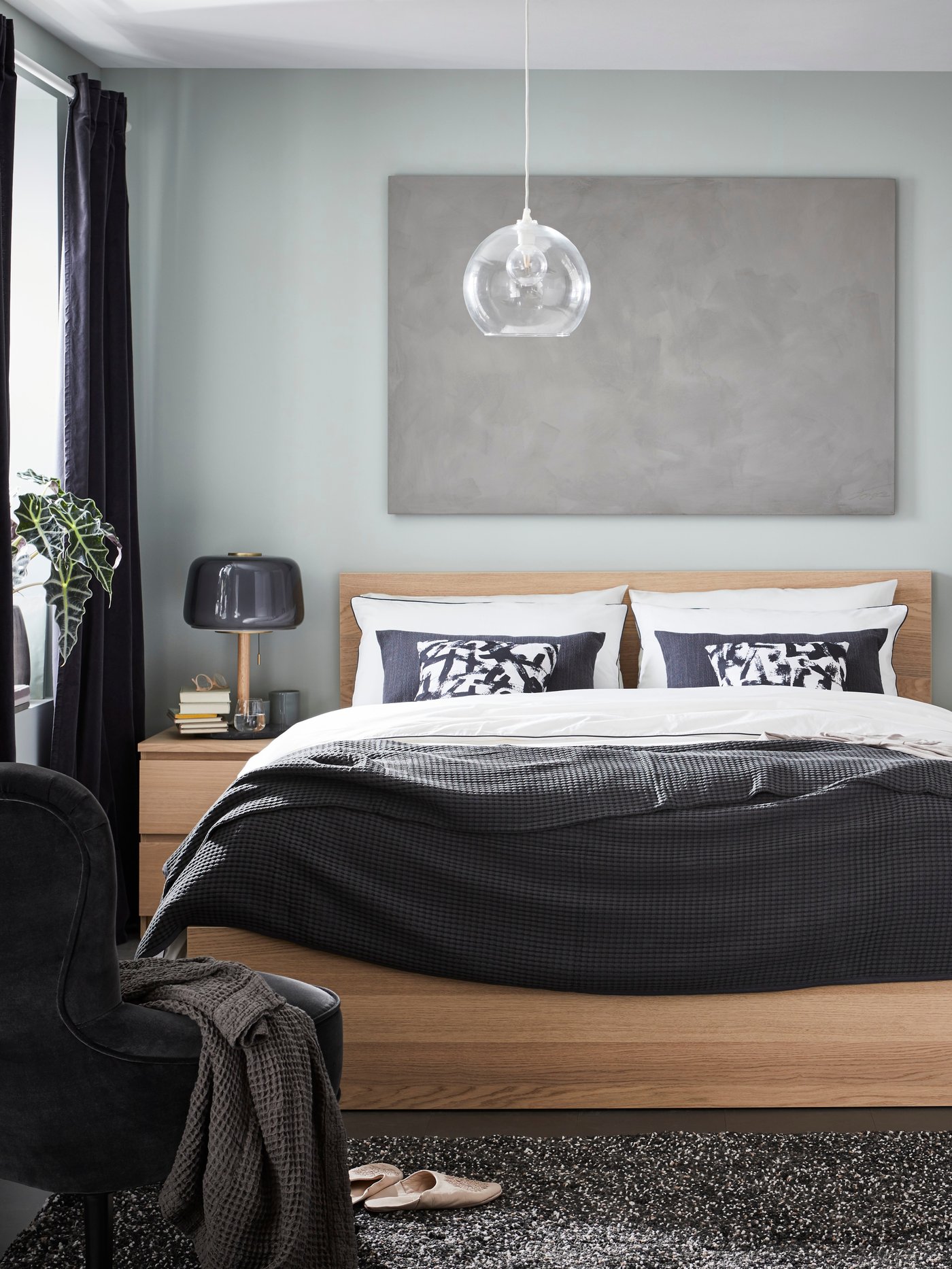 Estructura de cama alta MALM con tableros de roble pintados de blanco complementada con ropa de cama de colores claro y oscuro. Encima hay un cuadro gris.
