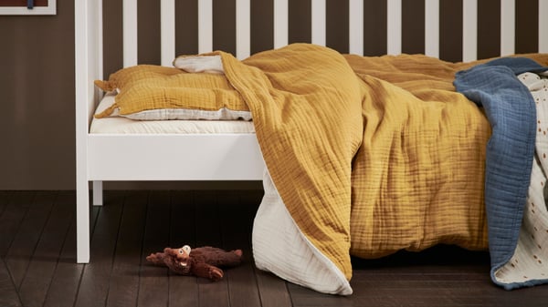 A dark yellow/beige GULDVÄVARE 3-piece bedlinen set for cot in the childrens room