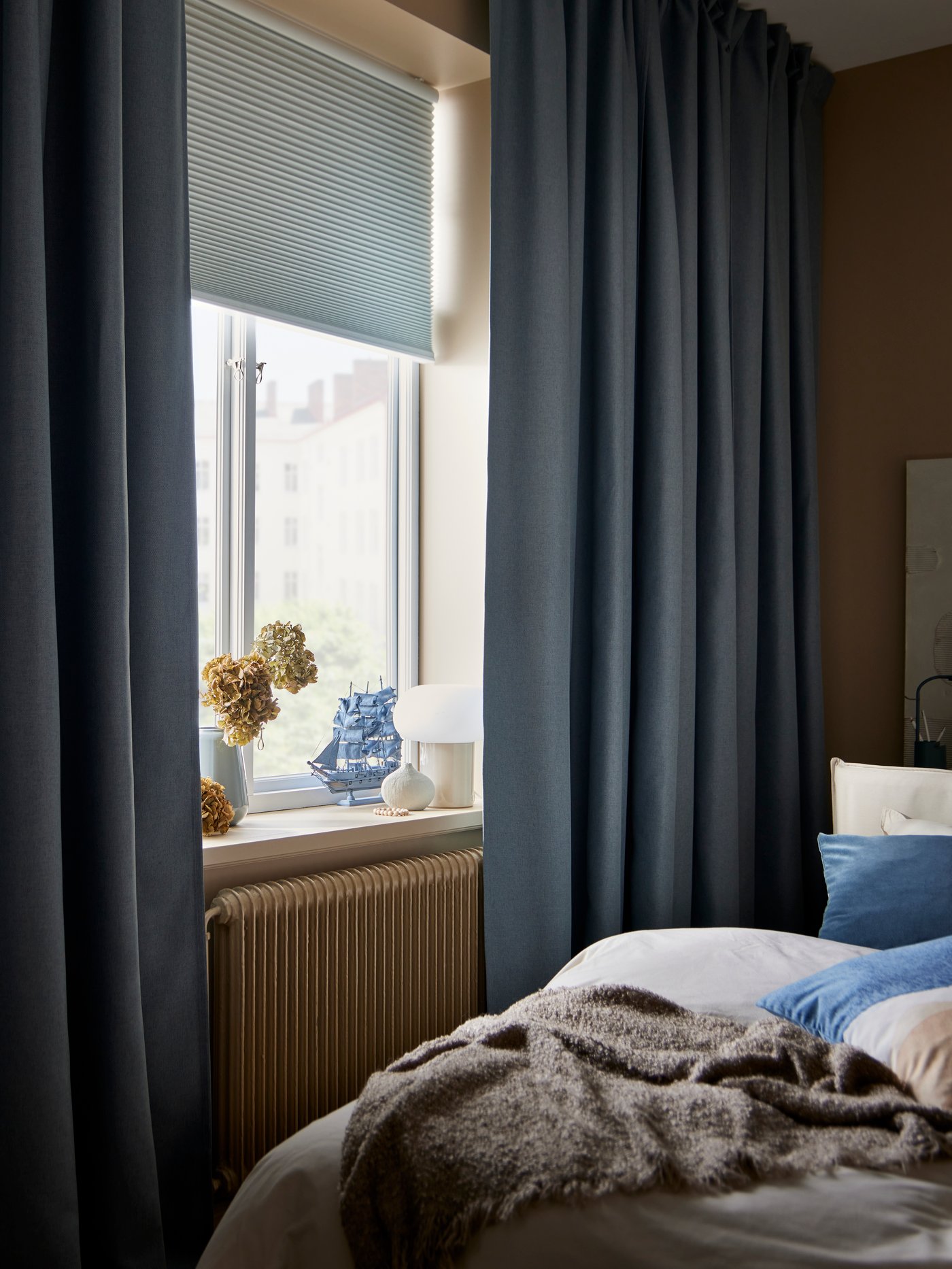 Gray curtains that are half drawn where the light comes in towards the bed.