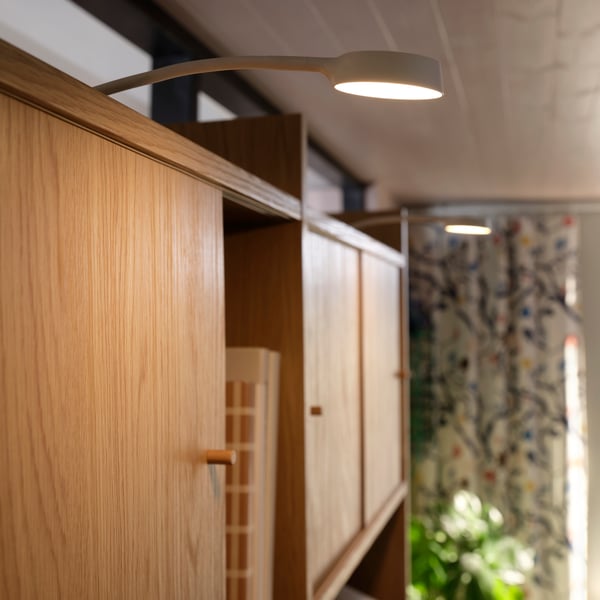 Lit YTBERG cabinet lighting mounted on top of a LÅDMAKARE storage combination with sliding doors in a light living room.