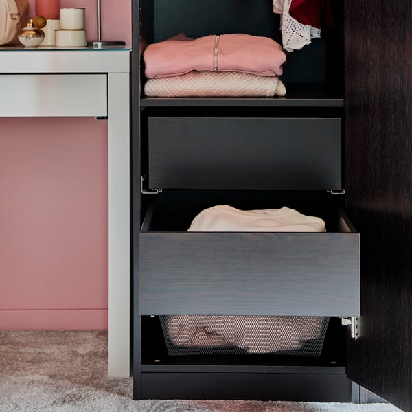 Ein Schlafzimmer, u. a. mit der KOMPLEMENT Schublade in Schwarzbraun vor einer rosafarbenen Wand