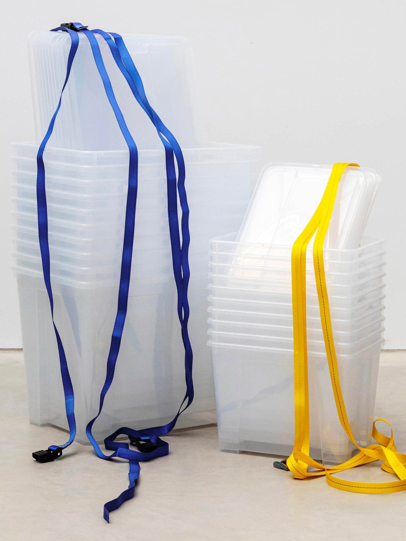Stapel transparenter IKEA SAMLA Boxen mit Deckeln, akzentuiert durch blaue und gelbe Gurtbänder.