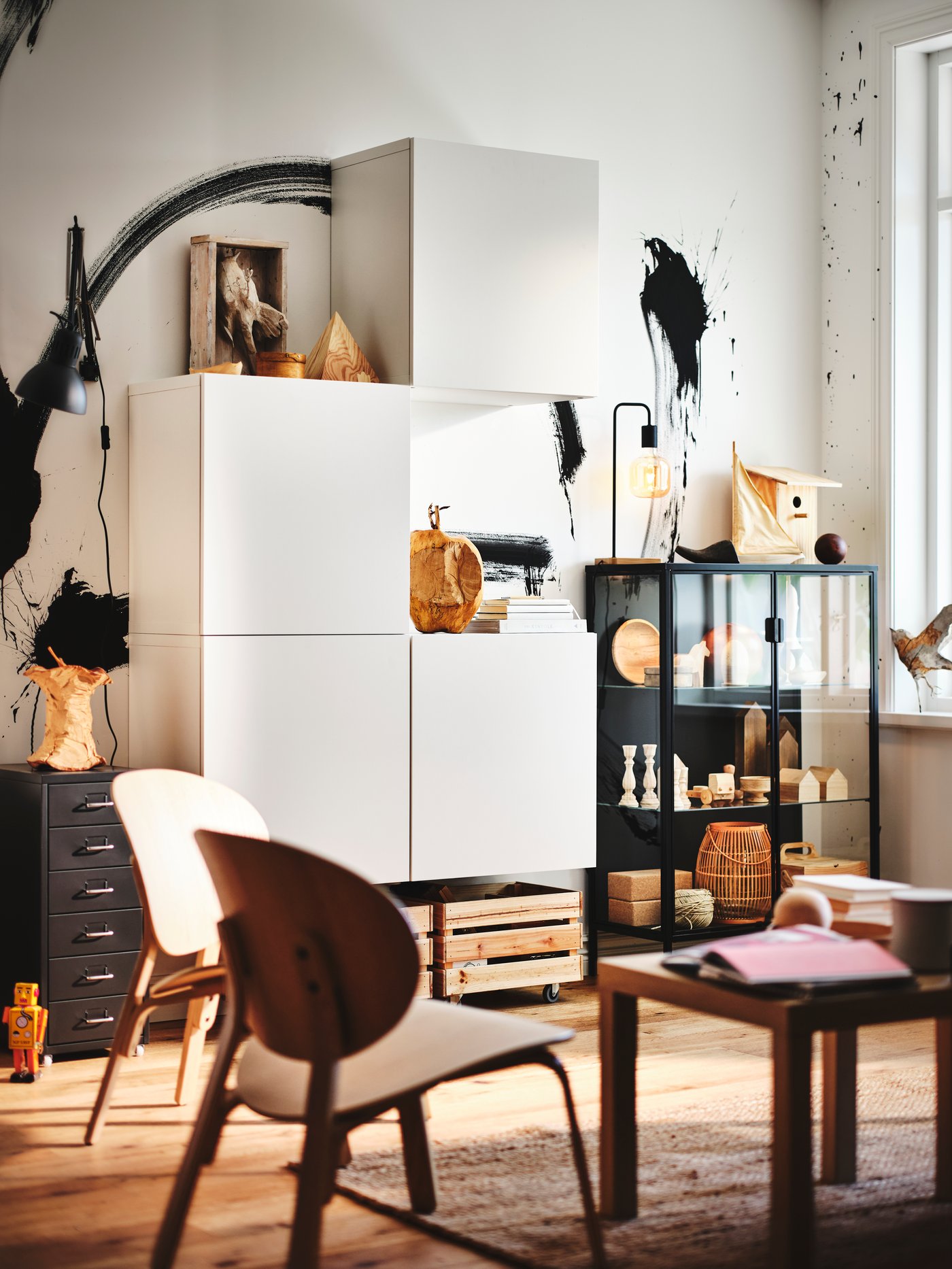 Un salón con estanterías BESTA con puertas montadas entre una cajonera negra y una vitrina gris con cajas.