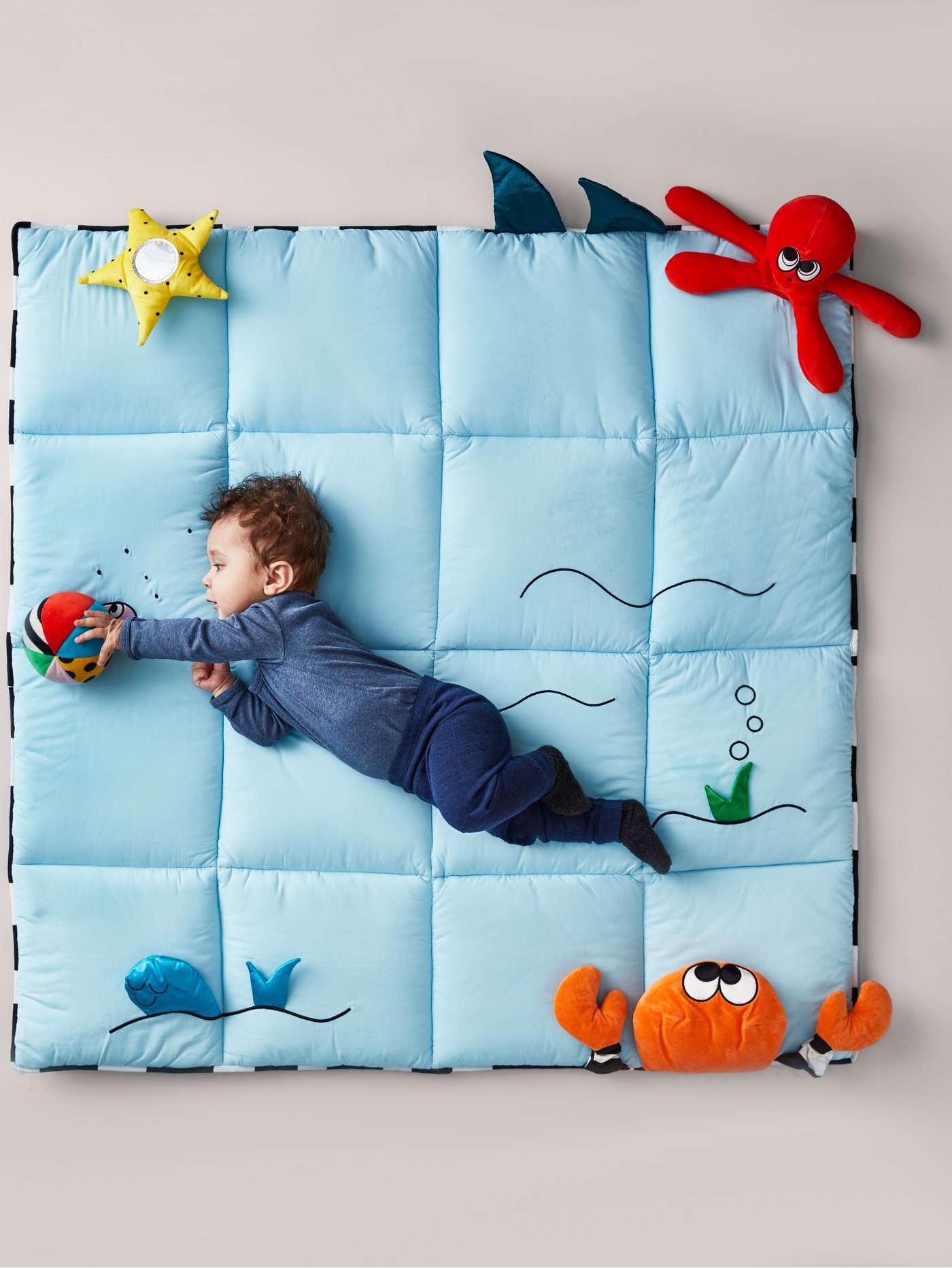 Gimnàs per a nadons de color blau i figures d'animals marins KLAPPA amb un nadó que juga ajagut a sobre.