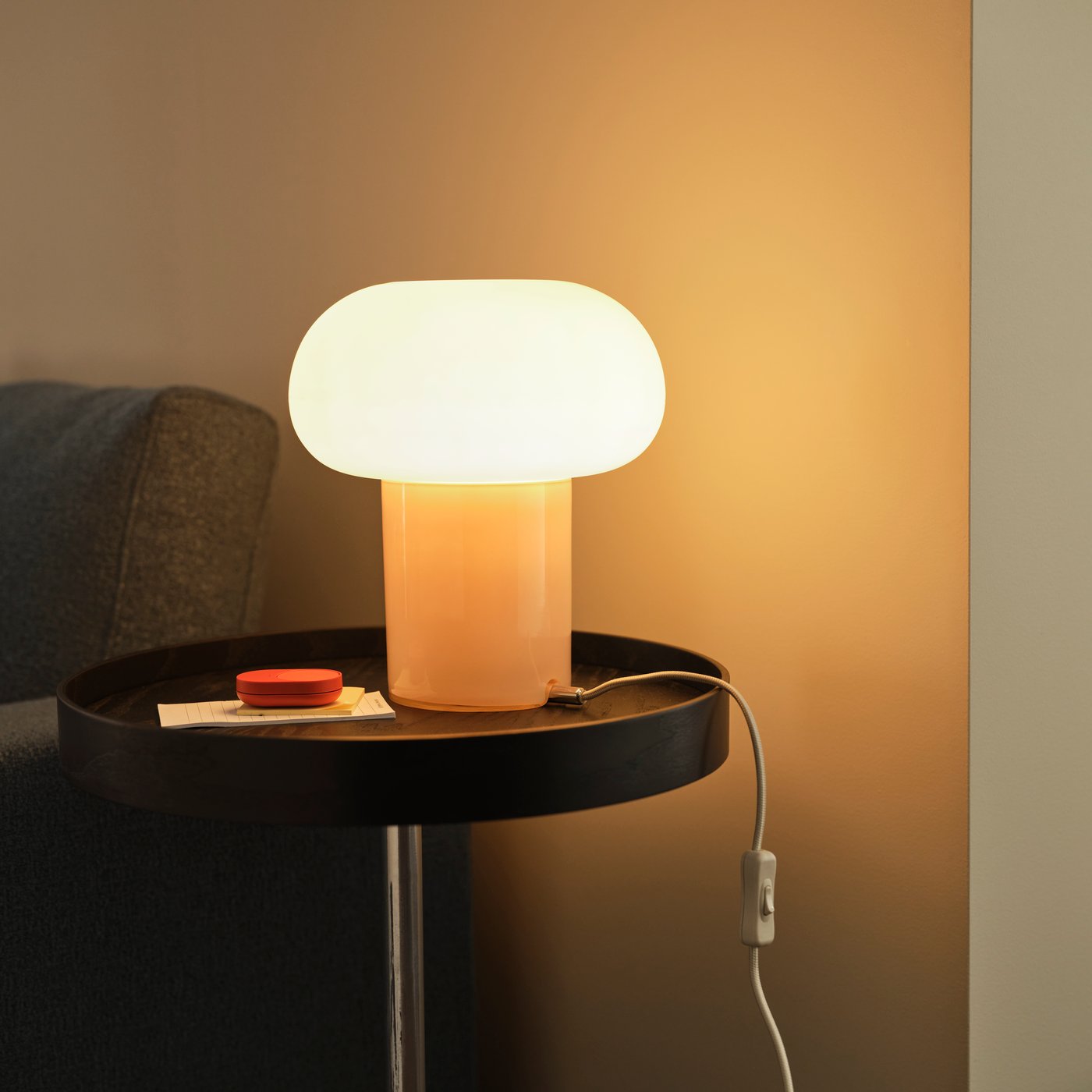 En DEJSA bordslampa står på ett svart TRANERED sidobord bredvid en BILRESA fjärrkontroll. Lampan är tänd.