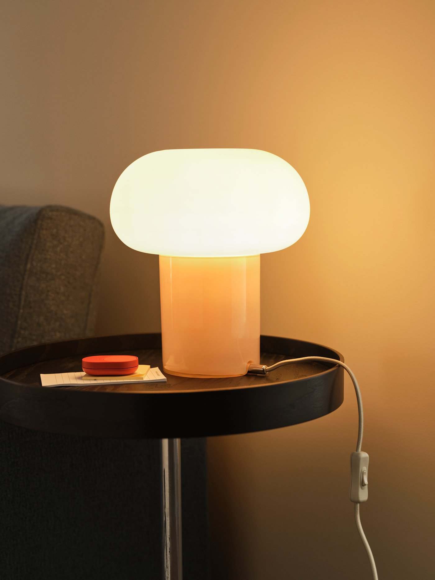A DEJSA table lamp stands on a black TRANERED side table beside a BILRESA remote control. The lamp is switched on.