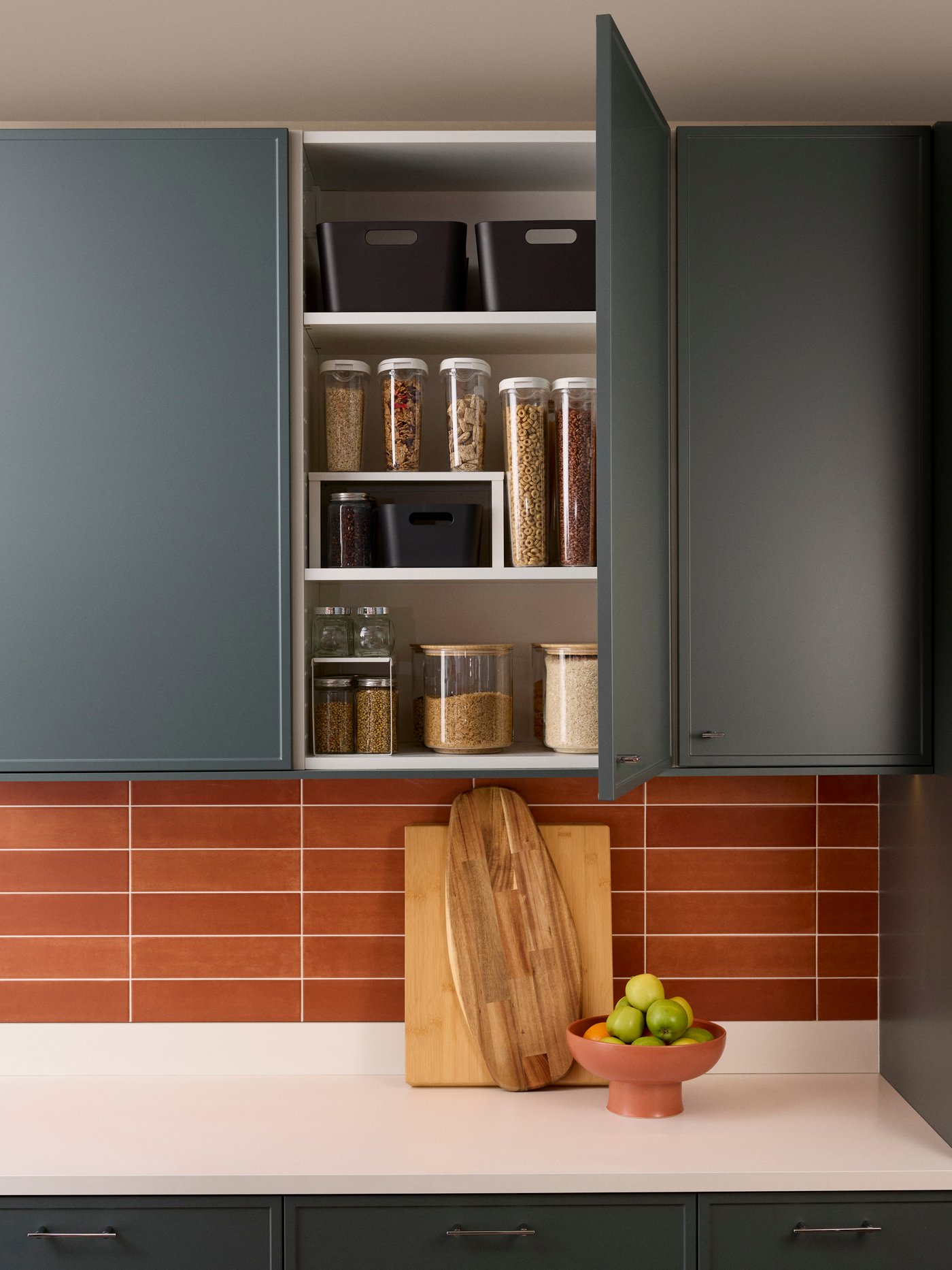 A close-up of a wall cabinet with the door ajar, showing inside transparent food containers well organised. The door is dark grey-green ASPUDDEN.