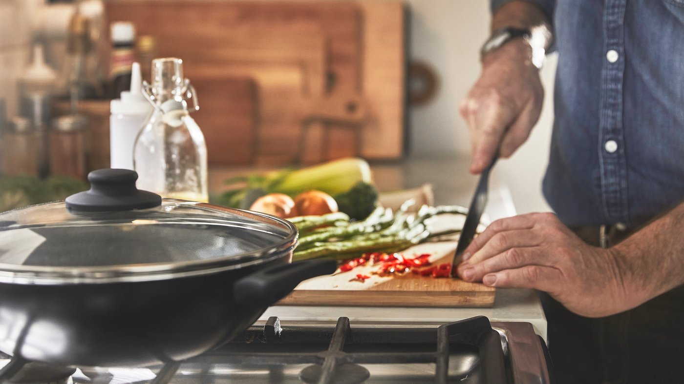 Main d'un homme coupant des légumes sur uen planche à découper en bois prêt d'un wok 