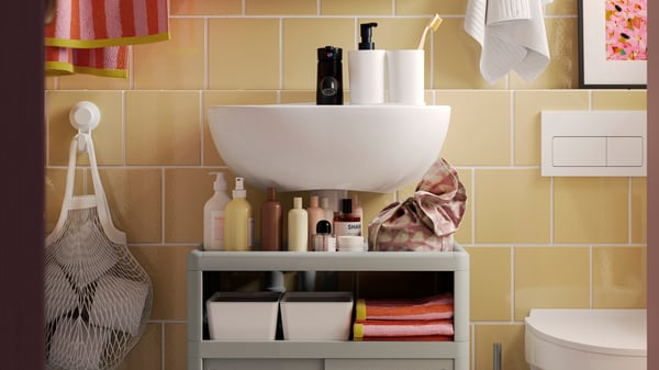 A white SKATSJÖN single wash-basin is mounted above a green IVÖSJÖN wash-basin base cabinet with bathroom products on it.