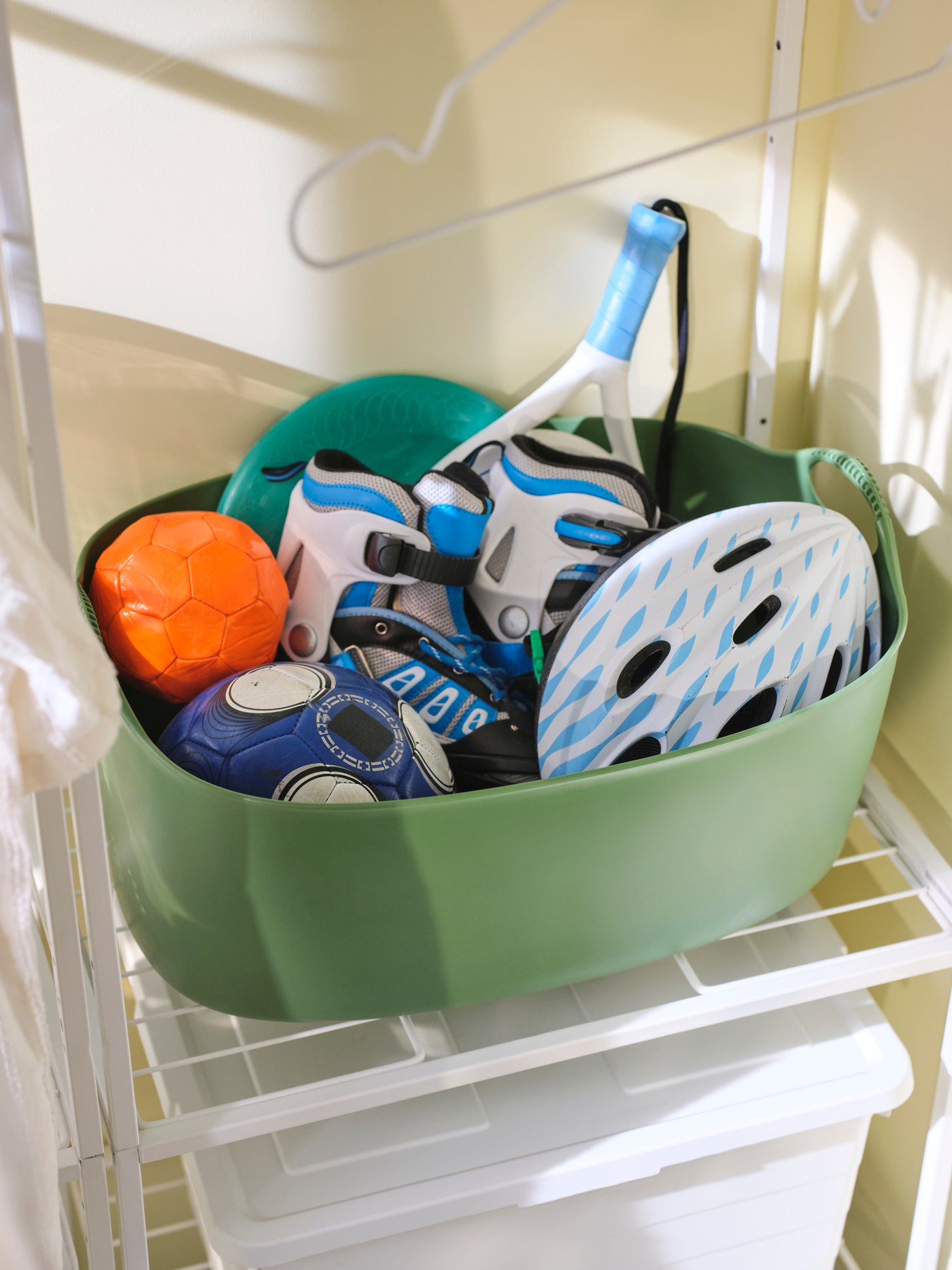 A big green plastic TORKIS flexi laundry basket is on a folding chair by a drying rack with pink fabric draped over its side.