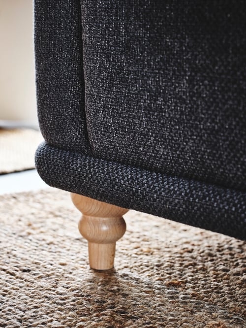 Close-up shot of an armchair’s lower corner, a wooden sofa leg, and a rectangular flatwoven rug in a living room.