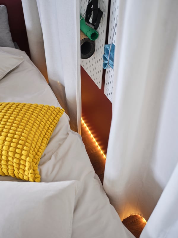 A close-up of one side of the guest bed and a hidden work out area behind the curtain. Mood lighting and a SKÅDIS pegboard.