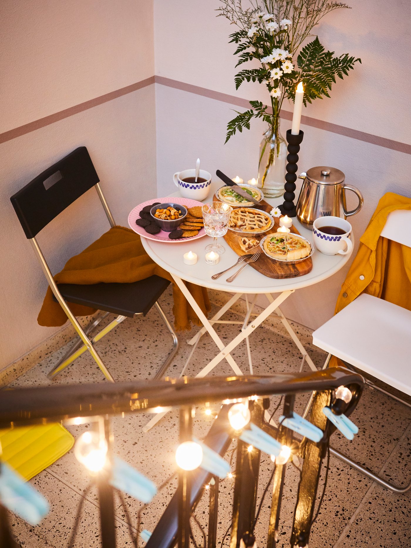 Inomhusbild med ett vitt bord, två fällstolar, en ljusstake, en kaffebryggare, tallrikar, bestick, ett glas och två kaffekoppar.