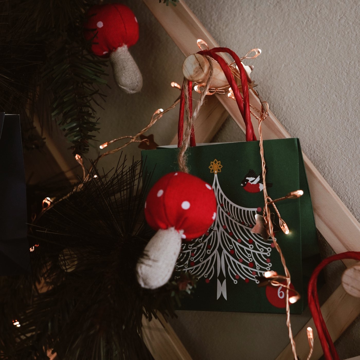 Scena natalizia con decorazioni a forma di funghi rossi e luci su un albero. Sullo sfondo c'è un sacchetto regalo verde con un motivo di alberi bianchi.