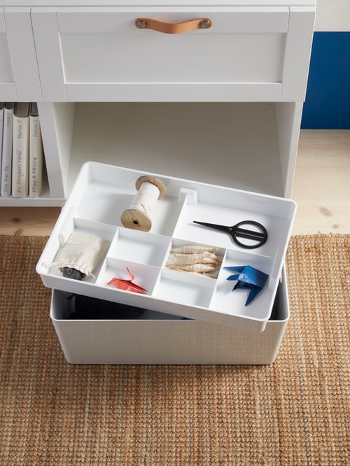 Workspace area featuring an insert with eight compartments containing items, placed on a container, which is set on a rug.
