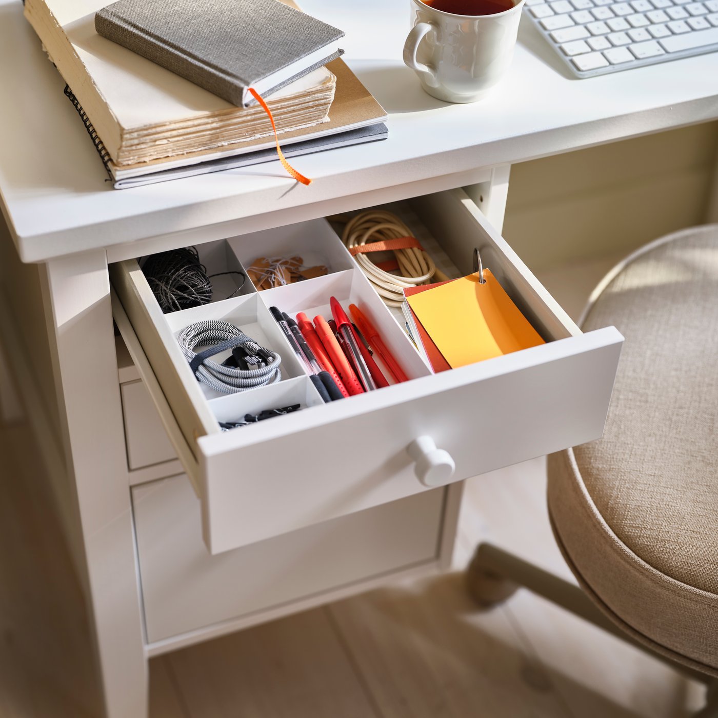 A teacup on a white GULLABERG desk with a drawer unit, the top drawer open to reveal neatly arranged accessories.