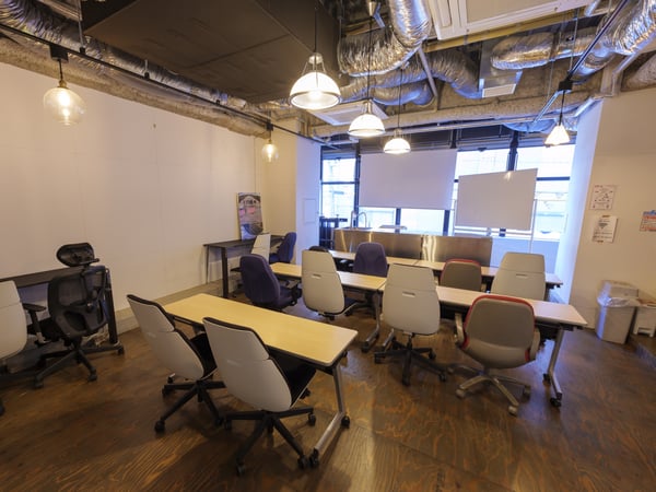 高天井と配管が特徴のオフィス。自然光が差し込む窓と整然と並ぶデスクが印象的な空間