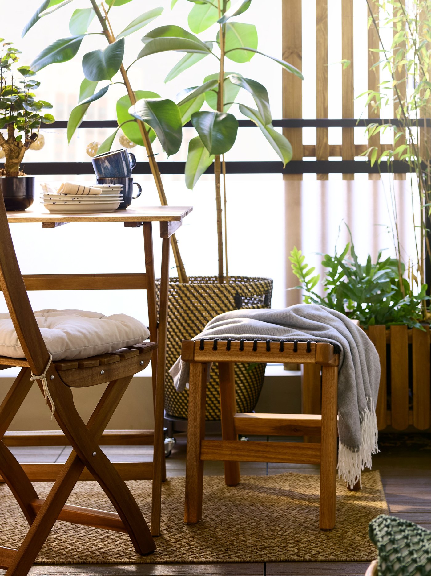 A light brown stained acacia ASKHOLMEN table and foldable chair face the view in a balcony with plants and natural materials.