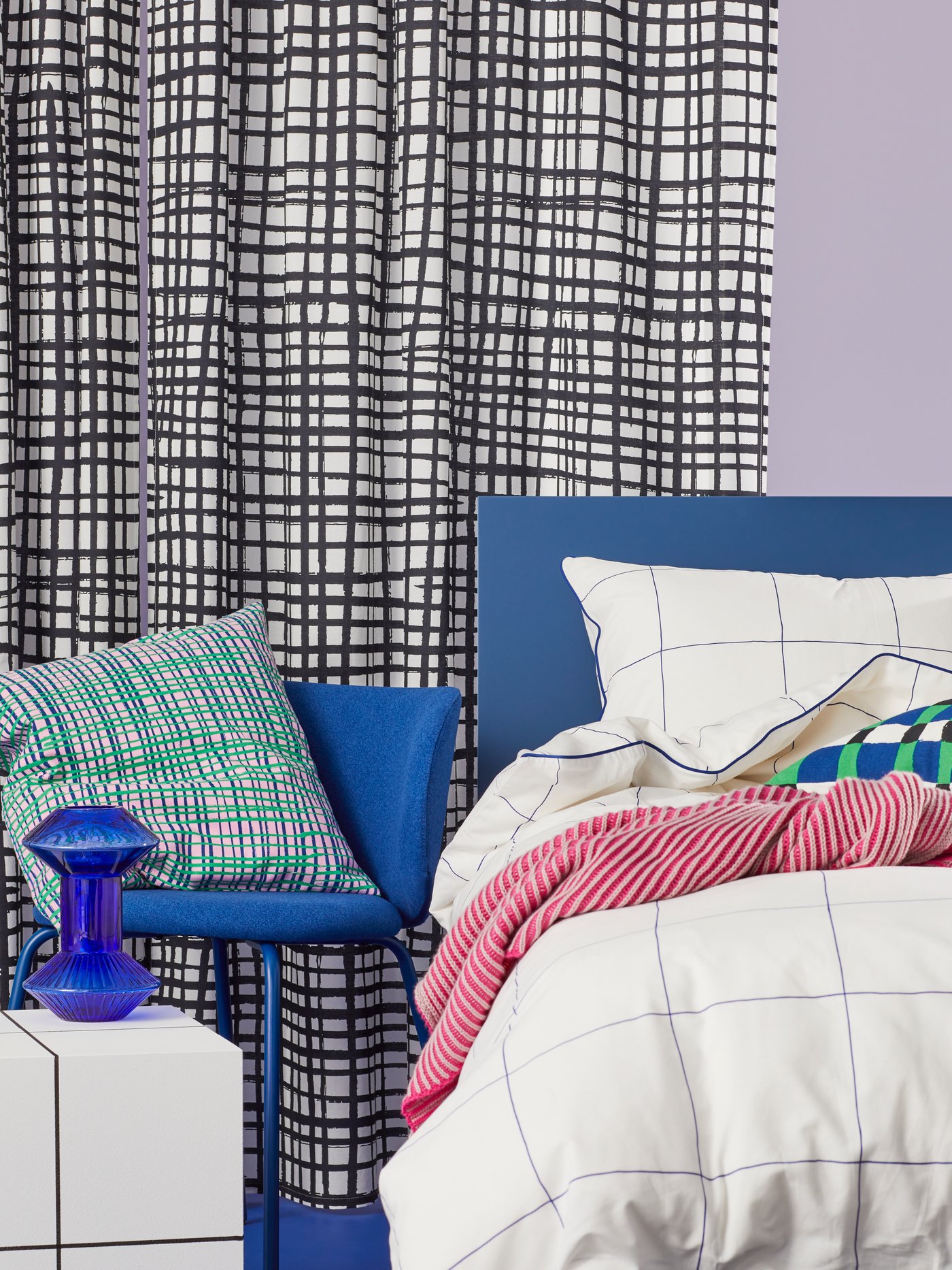 Close up of a bed with BREDVECKLARE duvet and pillow cover. To the right is a HAMNKRASSING cushion on a blue KRYLBO chair.