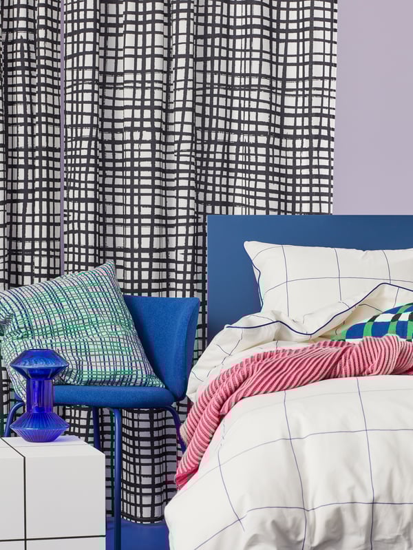 Detalle de una cama con fundas nórdica y de almohada BREDVECKLARE. A la derecha hay un cojín HAMNKRASSING sobre una silla KRYLBO azul.