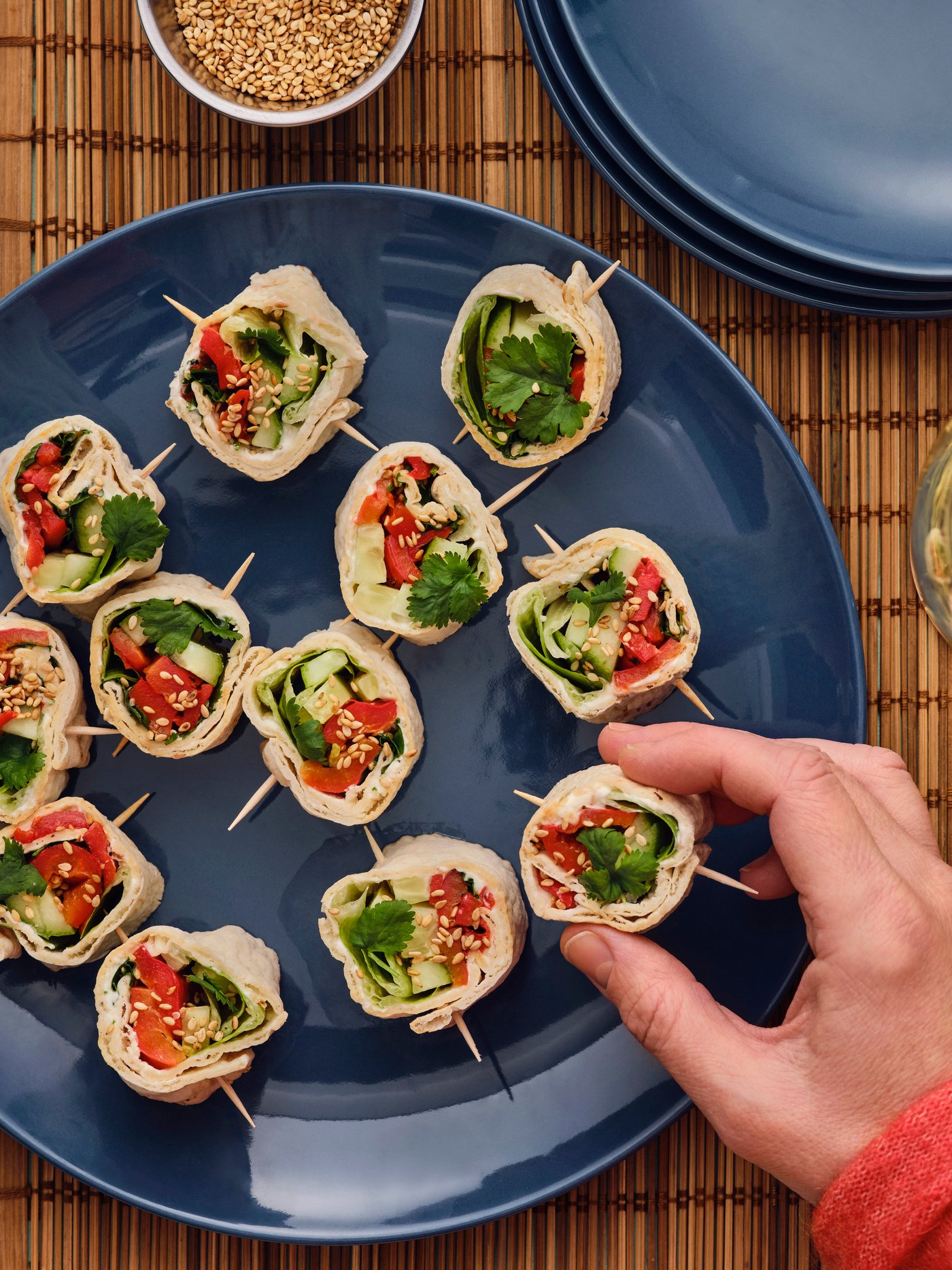 Eine Hand greift nach einem GRÄDDAT Fladenbrot mit gegrillter Paprika von einem Tisch mit Gläsern und blauen Tellern.