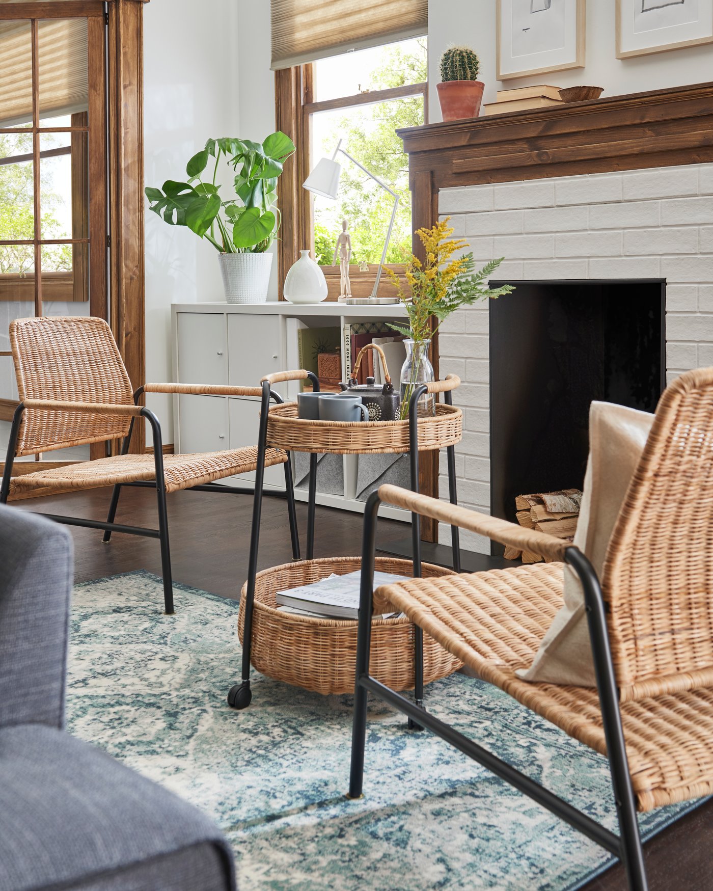 En sitthörna framför öppna spisen med två rottingfåtöljer, rottingbord och en blågrön matta. Detaljer som växter och glasföremål kompletterar den avslappnade stilen.