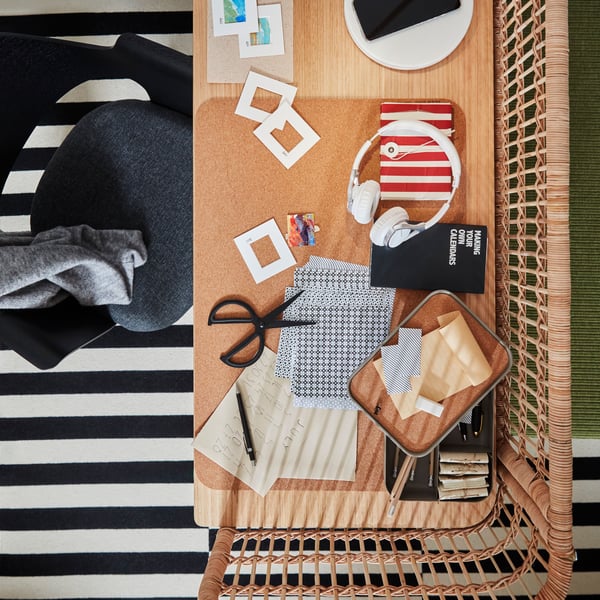 A black stained ash veneer FJÄLLBERGET conference chair with a grey seat at a rattan desk littered with craft materials.