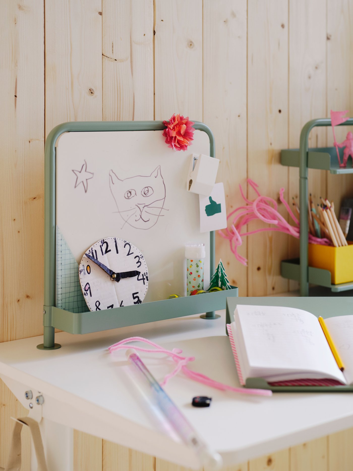 Tableau blanc et pupitre d’écriture RELATERA en gris-vert clair sur un bureau assis/debout RELATERA blanc. Un cahier est posé sur le pupitre.