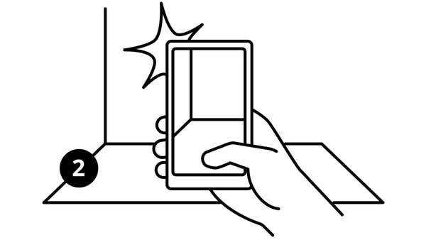 A black-and-white sketch, numbered two, of a hand holding up a mobile phone and snapping a picture of an empty room.