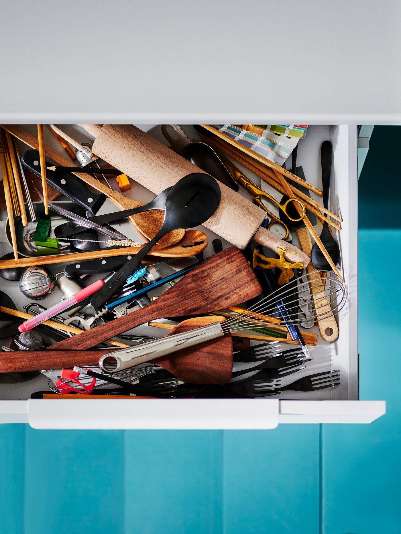 Odprt kuhinjski predal z neurejenim priborom.