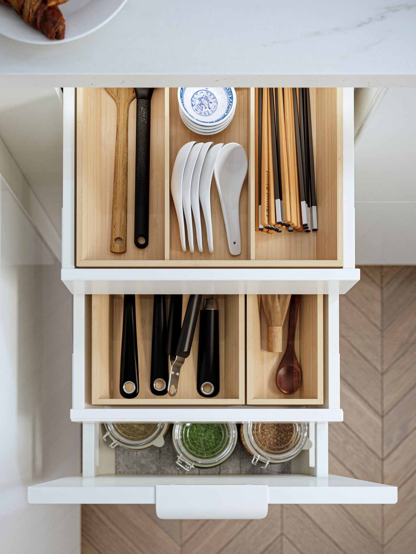 Un cajón de cocina abierto con organizadores de interior UPPDATERA de bambú claro con palillos y otros utensilios de cocina.
