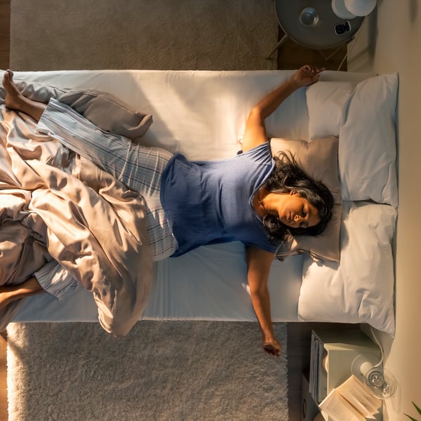 Von oben wird auf eine schlafende Person geblickt, die auf dem Rücken im Bett liegt und zum Teil von der Bettdecke in KRITSUGA Bettwäsche in Beige abgedeckt ist.