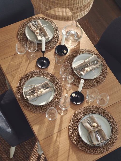 Overhead shot of three candlesticks with candles, place mats, plates, glasses, and cutlery, all of which are on a table.