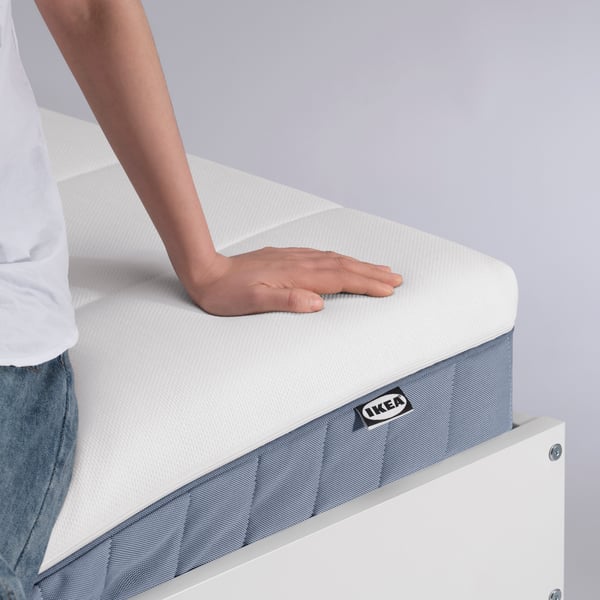 Close-up of a hand testing how soft an IKEA mattress is.