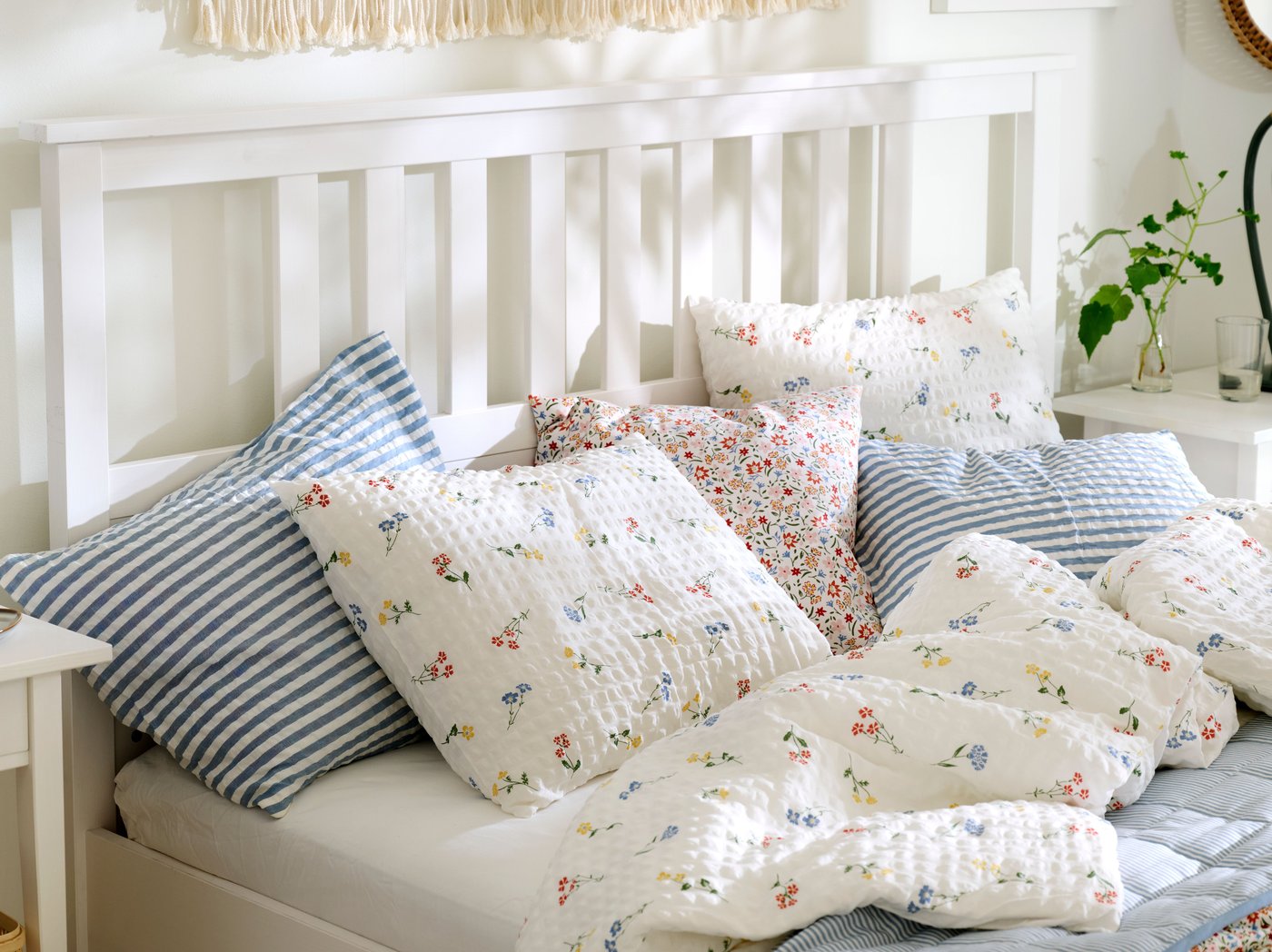 Close-up of a white HEMNES bed made with PILDVÄRGMAL duvet cover and pillowcases and bedding in other light colours.