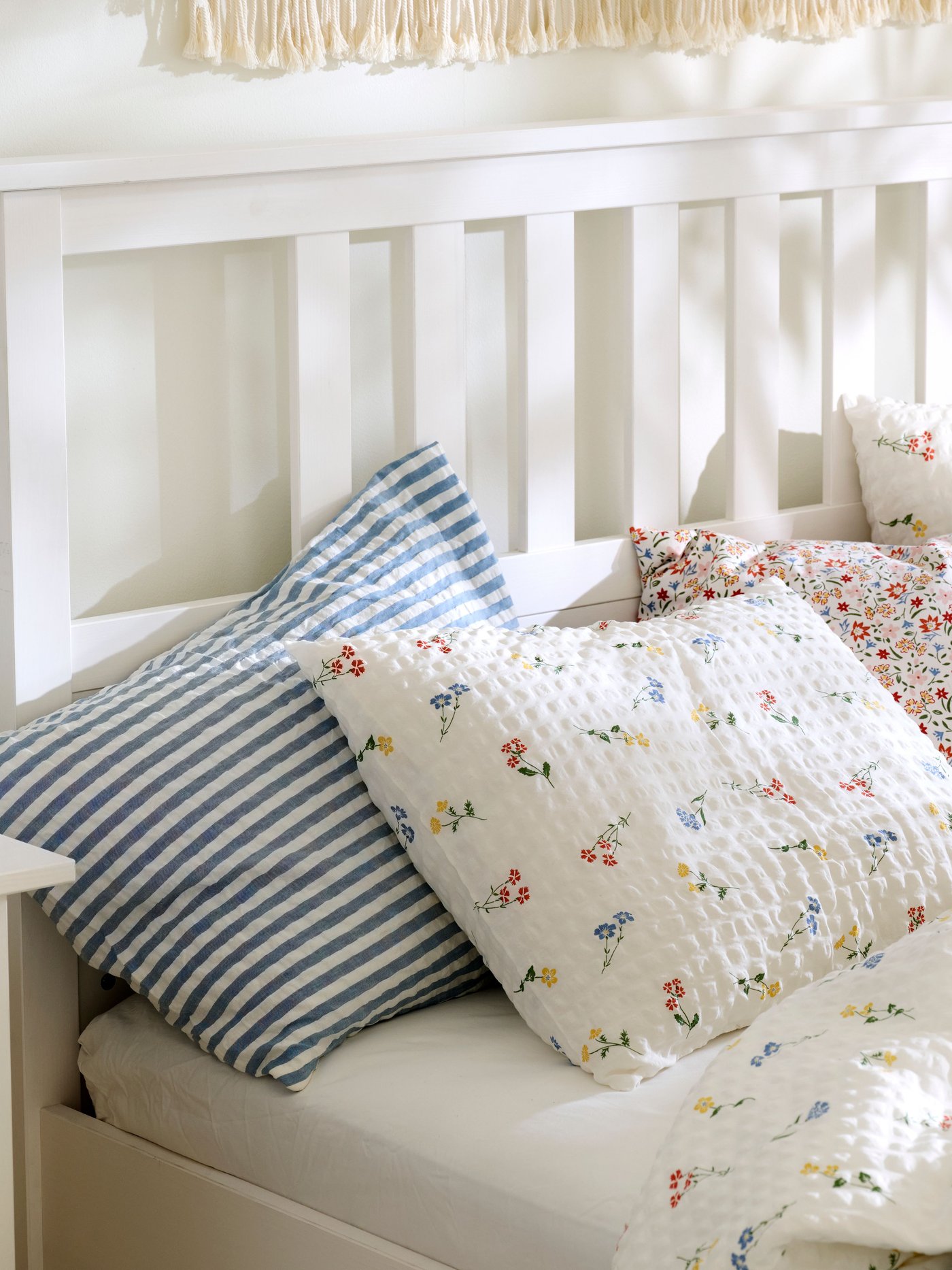 Close-up of a white HEMNES bed made with PILDVÄRGMAL duvet cover and pillowcases and bedding in other light colours.